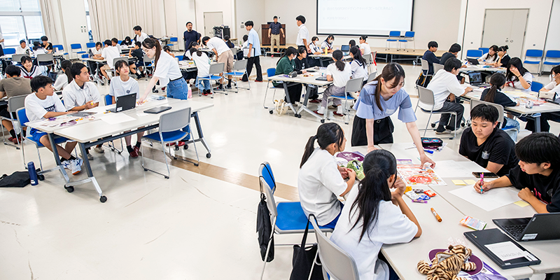 中高生合わせて60名以上が本庄高校の一室に集合。そこから4～5名の混合チームをつくり、POP を制作しました。